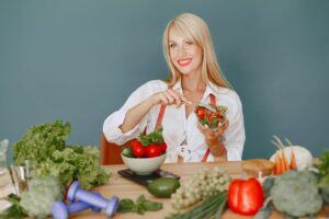 Woman Holding a Bowl with Salad while Sitting Behind a Table Full of Vegetables getting ready to prepare for a weight loss diet