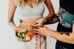 Man Measuring a Woman's Waistline Holding a Bowl of Salad