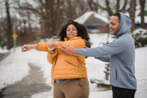 Positive African American overweight female in outerwear smiling while doing warming up exercise during personal training with coach