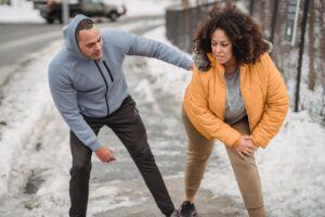 African American coach in sportswear helping plus size black female to warm up while standing on snowy pathway during training in winter time