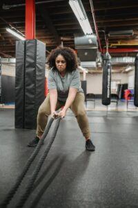 Full body focused African American female in sportswear exercising with battle ropes during functional workout in contemporary fitness center