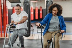 Plump black woman and muscular sportsman cycling in gym