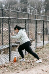 Side view of determined plus size female athlete in sportswear leaning on chain link fence while training in city park on cloudy autumn day
