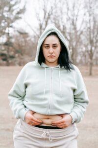Gloomy female in sportswear showing folds on waist and looking at camera while doing exercises in autumn day