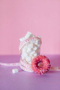 Blocks of Sugar on a Glass Beside a Donut on Pink Surface