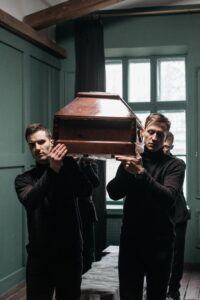A Group of Men in Black Clothing Carrying a Wooden Coffin