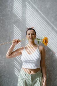 A Woman in White Tank Top Holding a Sunflower