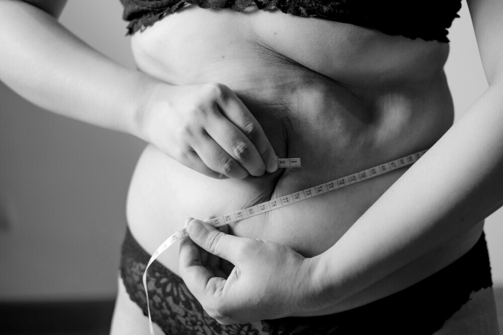 a woman is measuring her waist to check the progress of her weight as part of her weight loss strategies
